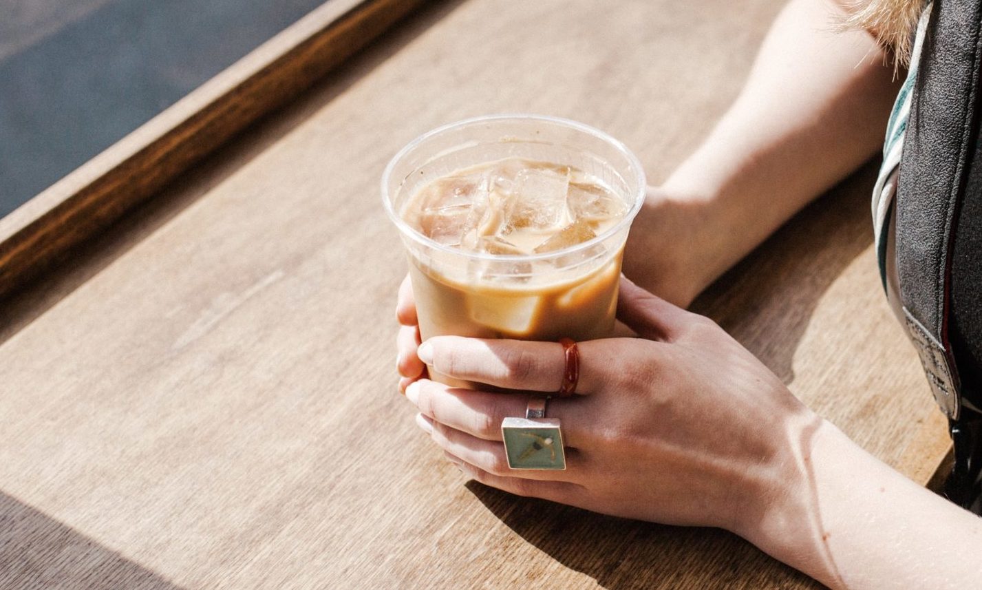 woman's hands holding iced latte coffee in plastic cup
